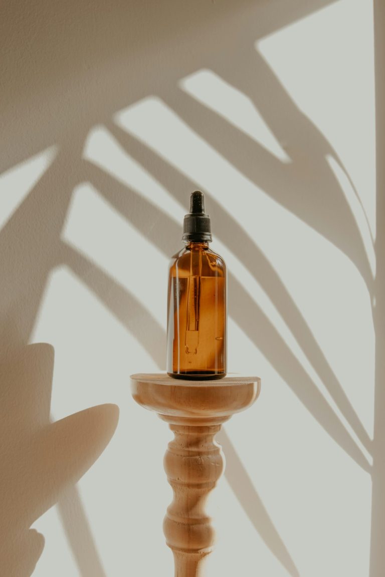 A plain amber dropper bottle on a wooden stand, with leaf shadows on the wall behind